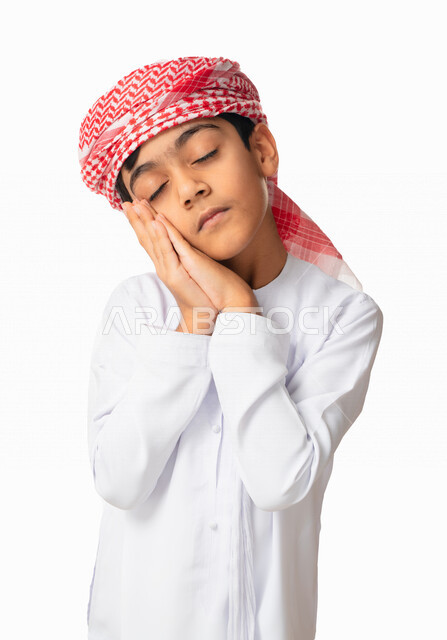 الشعور بالتعب و الحاجه الى النوم والراحه, الإحساس بالكسل و الإرهاق والخمول، بورتريه مقرب لولد عربي اماراتي خليجي يرتدي الكندورة والعمامة الاماراتية يضع يديه تحت رأسه, إيماءات وجه ويدين تدل على النعاس, خلفية بيضاء
