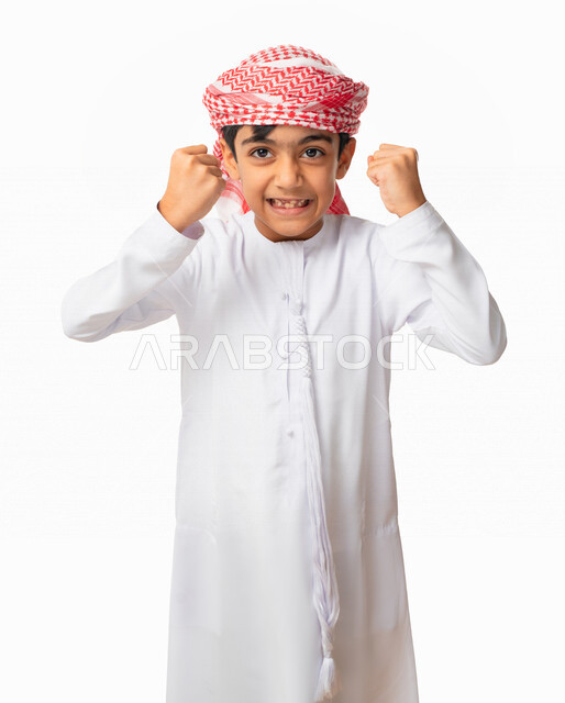 تحقيق الاهداف و إنجاز المهامات , بورتريه لولد عربي اماراتي خليجي يرتدي الكندورة والعمامة الاماراتية ويرفع يديه فرحا بالنصر, ايماءات وجه ويدين تدل على الفوز و الكسب, علامة الفرح والقوه, الإعجاب والرضا و الشعور بالسعاده، خلفية بيضاء