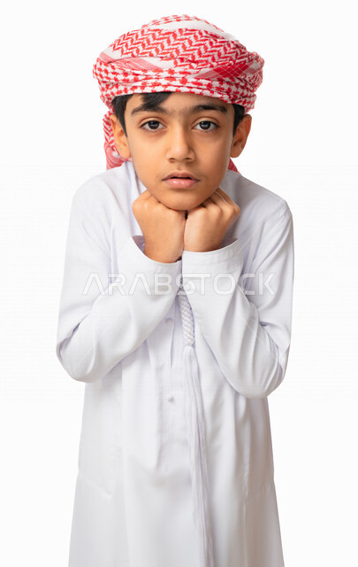 شرود الذهن والتفكير والتأمل, حركات يدين ووجه تدل على الخوف والرهبه ،بورتريه لولد عربي اماراتي خليجي يرتدي الكندورة والعمامة الاماراتية يضع يديه تحت ذقنه شعورا بالاحباط و الاستياء، مفهوم الشخصية الانطوائية،  خلفية بيضاء