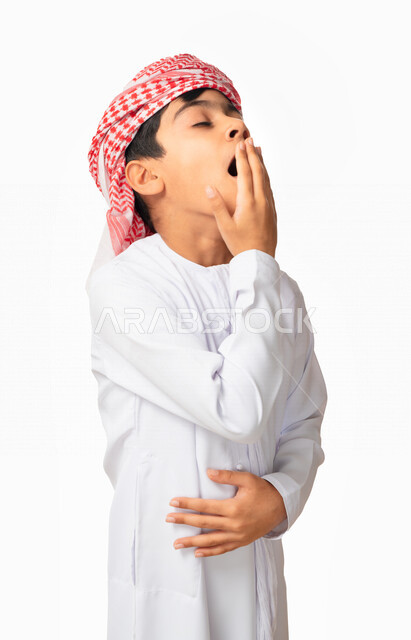 الكسل والخمول، الإحساس بالإرهاق و الحاجه الى النوم والراحه ,بورتريه لولد عربي اماراتي خليجي يرتدي الكندورة والعمامة يضع يده على فمه ،إيماءات وجه ويدين تدل على النعاس, التثاؤب و الشعور بالتعب، خلفية بيضاء