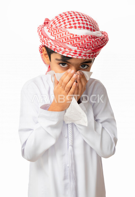 التهابات الأنف التحسسية,  الحاجة الى العلاج والدواء, استخدام المناديل الورقيه للعطس, بورتريه لطفل عربي اماراتي خليجي يرتدي العمامة والكندورة بإيماءات وجه ويدين تدل على العطاس, الشعور بالمرض و الزكام, خلفية بيضاء