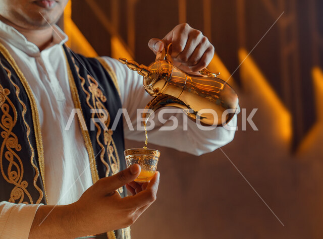 صورة مقربة لرجل عربي يقوم بصب القهوه العربية، تقديم القهوة الساخنة للضيوف، إكرام الضيف، دلة قهوة عربية، الضيافة السعودية، القهوة العربية، حسن الضيافه والإستقبال، والترحيب بالضيوف، أعياد ومناسبات