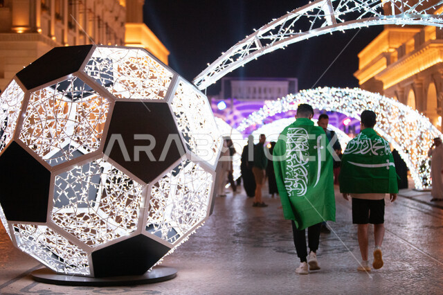 أشخاص يمشون بجوار كرة قدم مضيئة قبل بطولة كأس العالم لكرة القدم 2022 في قرية كتارا الثقافية في الدوحة، قطر، 15 نوفمبر 2022، علم السعودية،  كأس العالم في قطر 2022، بطولة كأس العالم، فيفا 2022، مونديال قطر