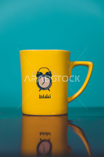 صورة مقربة لكوب اصفر اللون، فنجان اصفر فارغ، رسمة لساعة تنبيه، كوب زجاجي، كلمة نشاط، خلفية زرقاء