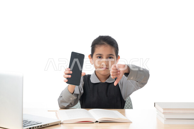 ايماءات وجه ويدين تدل على عدم الإعجاب، سلبيات التعلم عن بعد باستخدام وسائل التكنولوجيا الحديثة، بورتريه لطالبة عربية خليجية اماراتية ترتدي اليونيفورم المدرسي تمسك بيدها الهاتف المحمول، تلميذة سعودية  تشير إلى الأسفل بإصبع الابهام، خلفية بيضاء