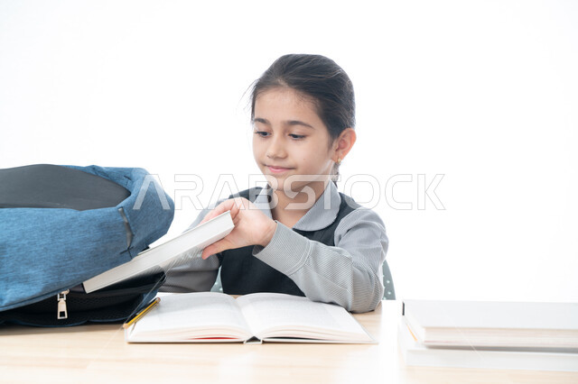 الاجتهاد والتفوق ومتابعة الدراسة، بورتريه لتلميذة عربية خليجية اماراتية ترتدي اليونيفورم المدرسي تقوم بسحب الكتب من الحقيبة، تجهيز الطاولة الدراسية لمراجعة الدروس، طالبة سعودية متحمسة للقراءة والحفظ وإنهاء الواجبات المنزلية المطلوبة، خلفية بيضاء