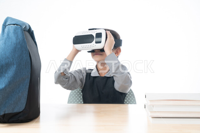 طرق تعليمية جديدة، جمع التعلم مع الترفيه باستخدام التقنية الحديثة، بورتريه لتلميذة عربية خليجية اماراتية ترتدي الزي المدرسي تمسك بيديها نظارات العالم الافتراضي التعليمي، طالبة سعودية تجلس على طاولة الدراسة تضع بجانبها الحقيبة المدرسية، خلفية بيضاء