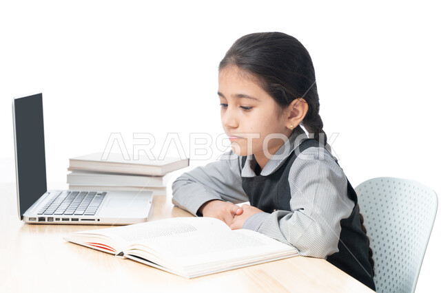 Following classes and homework online, a close-up portrait of a Gulf Arab Emirati student wearing a school uniform and studying at home, studying and studying remotely, the concept of e-learning, a diligent Saudi student reviewing her lessons from books a