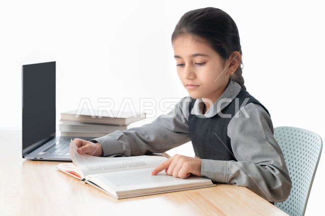 حل  الواجبات و متابعة الحصص عبر الانترنت، بورترية مقرب لتلميذة خليجية عربية إماراتية ترتدي مريول المدرسة و تدرس في المنزل، المذاكرة و الدراسة عن بعد، مفهوم التعليم الإلكتروني، طالبة سعودية مجتهدة تراجع دروسها من الكتب وتستخدم الحاسوب المحمول،  خلفية بيضاء