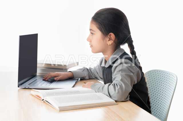 Doing homework and following classes online, a close-up portrait of a Gulf Arab Emirati student wearing a school uniform and studying at home, studying and studying remotely, the concept of e-learning, a diligent Saudi student reviewing her lessons from b