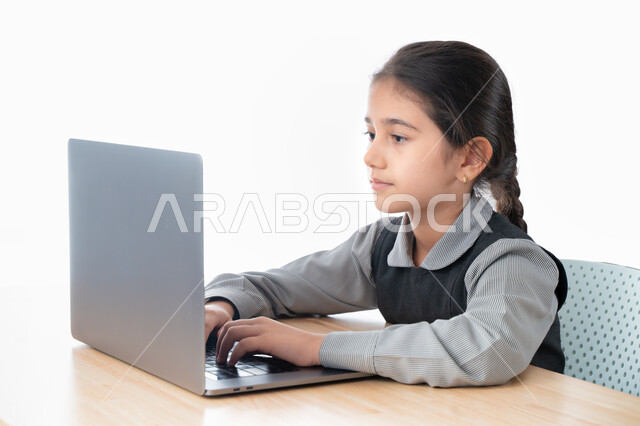 The concept of studying and persevering in progress and success, a close-up portrait of a Gulf Arab Emirati student wearing a school uniform and following online classes via the computer, a diligent and outstanding Saudi student studying remotely via the 