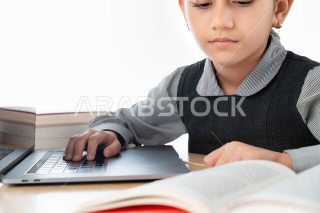 المذاكرة و الدراسة عن بعد، بورترية مقرب لتلميذة خليجية عربية إماراتية ترتدي مريول المدرسة و تدرس في المنزل، مفهوم التعليم الإلكتروني، طالبة سعودية مجتهدة تراجع دروسها من الكتب وتستخدم الحاسوب المحمول، متابعة الحصص و حل الواجبات عبر الانترنت، خلفية بيضاء