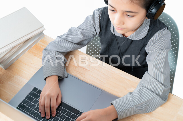  التحضير للإمتحانات و الإختبارات النهائية، طالبة سعودية تذاكر دروسها من الحاسوب، بورترية مقرب لتلميذة خليجية عربية إماراتية ترتدي الزي المدرسي و سماعة الرأٍس، حضور البث المباشر للحصص الاونلاين عن طريق الكمبيوتر، مفهوم التعليم الإلكتروني، خلفية بيضاء