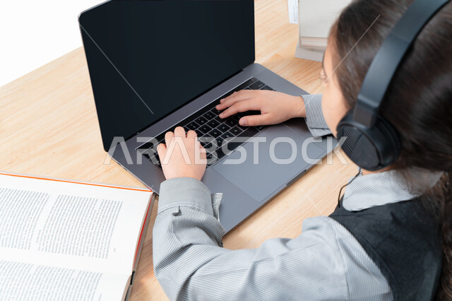 Attending the live broadcast of the online classes via the computer, a close-up portrait of a Gulf Arab Emirati student wearing a school uniform and a headphone, the concept of e-learning, a Saudi student studying her lessons tickets from the computer, pr
