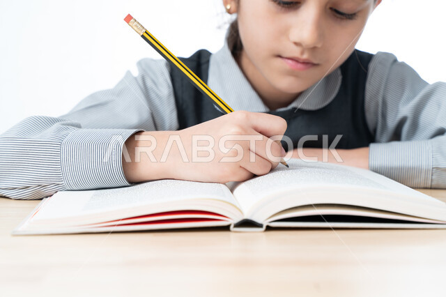 Gaining knowledge from writing homework and doing effective educational tasks, a close-up portrait of an Arab Gulf Emirati student wearing a school apron and sitting at the study table, a Saudi student writing down information to enable and understand les