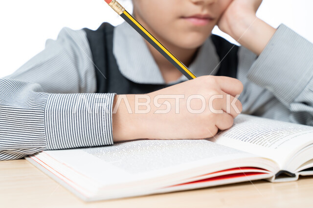 المعرفة المكتسبة من كتابة الواجبات والقيام بالمهام التعليمية الفعالة, بورتريه مقرب لطالبة عربية خليجية إماراتية ترتدي المريول المدرسي وتجلس على طاولة الدراسة, تلميذة سعودية تقوم بتدوين المعلومات لتمكين وفهم الدروس, خلفية بيضاء