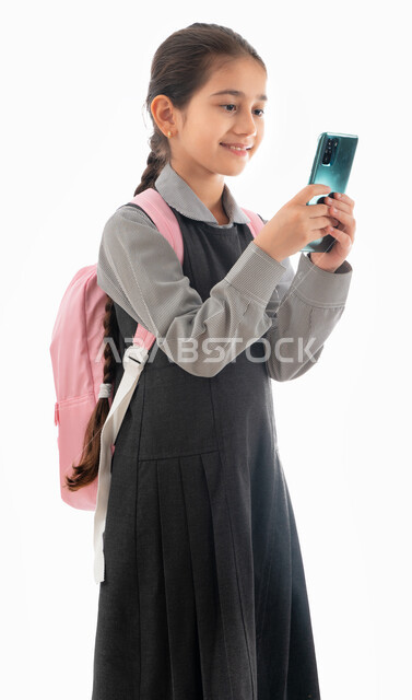 مشاركة مشاعر السرور لبدء العام الدراسي, بورتريه لطالبة عربية خليجية إماراتية ترتدي اليونيفورم المدرسي وحقيبة الظهر  تستخدم الهاتف المحمول في الدراسة وحل الواجبات, تلميذة سعودية تقوم بإجراء بحث عبر الانترنت, استخدام التكنولوجيا في التعليم، خلفية بيضاء