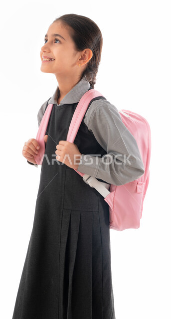 Preparing for the new school year, a portrait of an Arab Gulf Emirati student wearing a school uniform and a school backpack, a smiling, diligent, polite Saudi student who loves studying, looking at something, gestures indicating pleasure and enthusiasm f