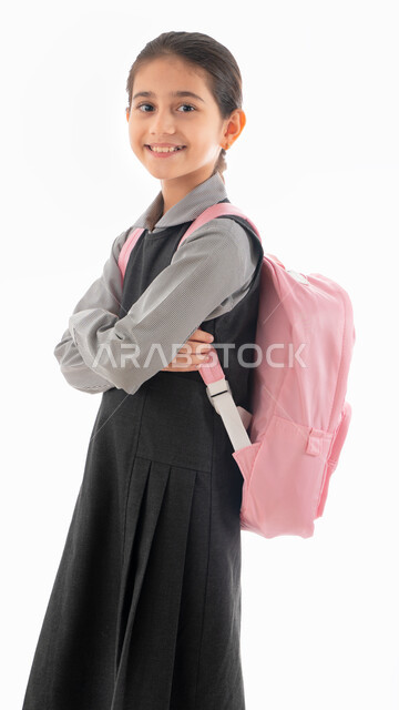 حب التعلم والتعليم, ايماءات الأدب والأخلاق المهذبه, العوده إلى المدارس, بورتريه لطالبة عربيه خليجية اماراتية ترتدي المريول المدرسي وتحمل حقيبة الظهر المدرسية, تلميذه سعودية مكتفة اليدين تبتسم وتنظر إلى الكاميرا, الإستعداد للعام الدراسي الجديد, خلفية بيضاء