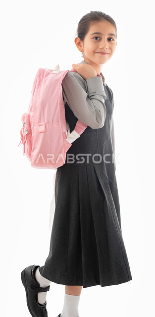 التهيئة والتجهيز لبداية العام الدراسي, بورتريه من الجانب لطالبة عربية خليجية اماراتية ترتدي الزي المدرسي وتحمل الحقيبة المدرسية, تلميذه سعودية تبتسم وتنظر للكاميرا, ايماءات المشي إلى المدرسه, موسم العوده للمدارس, صورة الجسم بالطول الكامل, خلفية بيضاء.