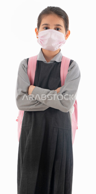 العوده بحذر للدراسه الحضوريه في المدارس, الوعي الصحي وتجنب إنتشار العدوى, بورتريه لتلميذة عربية خليجية اماراتية ترتدي الزي المدرسي وتحمل الحقيبة المدرسية, طالبه سعودية تضع الكمامة وتنظر إلى الكاميرا, الوقاية من فايروس كورونا, خلفيه بيضاء.