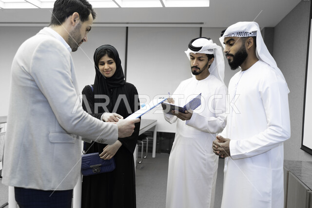 صورة بلون الابيض و الأسود لمدرب  يشرح لطلاب وطالبات عرب خليجيين و إماراتين  المحاضره, مدرب جامعي,طلاب إماراتيون يقفنا أمام بروفيسور جامعة ويتم   تدوين الملاحظات على جهاز الحاسب و دفتر الملاحظات , التعليم الجامعي في الإمارات العربية المتحدة , فريق عمل عربي