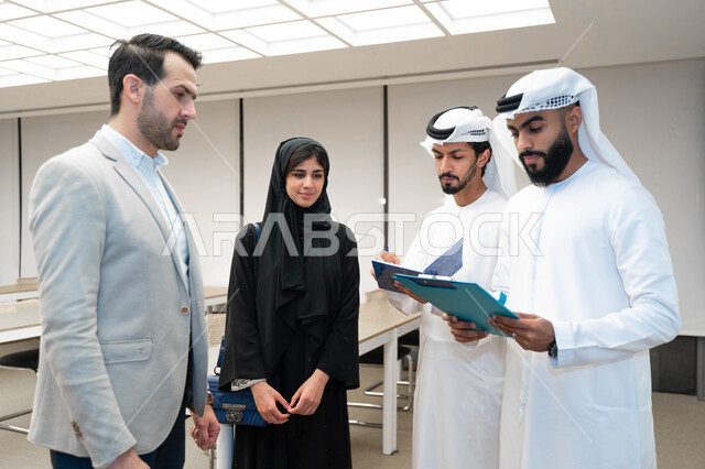 مدرب  يشرح لطلاب وطالبات عرب خليجيين و إماراتين  المحاضره, مدرب جامعي,طلاب إماراتيون يقفنا أمام بروفيسور جامعة ويتم   تدوين الملاحظات على جهاز الحاسب و دفتر الملاحظات , التعليم الجامعي في الإمارات العربية المتحدة , فريق عمل عربي إماراتي  خليجي