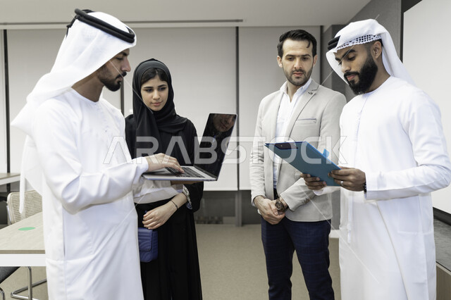 صورة بلون الابيض و الأسود لمدرب  يشرح لطلاب وطالبات عرب خليجيين و إماراتين  المحاضره, مدرب جامعي,طلاب إماراتيون يقفنا أمام بروفيسور جامعة ويتم   تدوين الملاحظات على جهاز الحاسب و دفتر الملاحظات , التعليم الجامعي في الإمارات العربية المتحدة , فريق عمل عربي