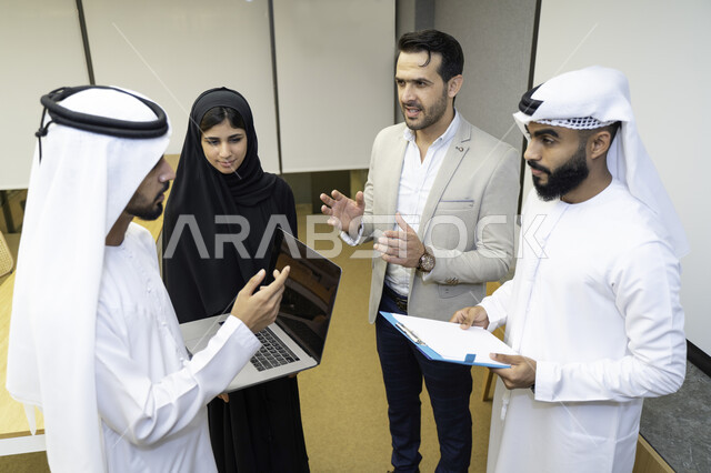 مدرب  يشرح لطلاب وطالبات عرب خليجيين و إماراتين  المحاضره, مدرب جامعي,طلاب إماراتيون يقفنا أمام بروفيسور جامعة ويتم   تدوين الملاحظات على جهاز الحاسب و دفتر الملاحظات , التعليم الجامعي في الإمارات العربية المتحدة , فريق عمل عربي إماراتي  خليجي