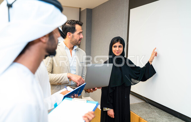 أستاذه جامعيه عربيه إماراتية خليجيه تشرح لطلابها المحاضره, مدربه جامعيه,طلاب إماراتيون يقفنا أمام الأستاذة ويتم  تدوين الملاحظات على جهاز الحاسب , التعليم الجامعي في الإمارات العربية المتحدة , فريق عمل عربي إماراتي  خليجي