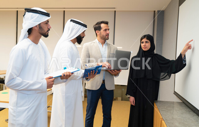 أستاذه جامعيه عربيه إماراتية خليجيه تشرح لطلابها المحاضره, مدربه جامعيه,طلاب إماراتيون يقفنا أمام الأستاذة ويتم  تدوين الملاحظات على جهاز الحاسب , التعليم الجامعي في الإمارات العربية المتحدة , فريق عمل عربي إماراتي  خليجي