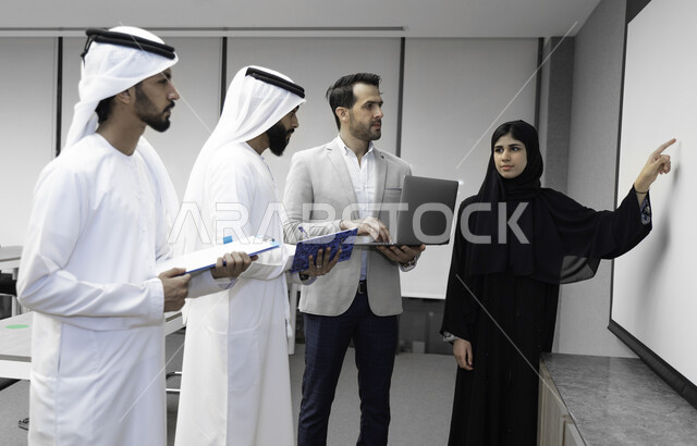 صورة بلون الابيض والاسود لأستاذه جامعيه عربيه إماراتية خليجيه تشرح لطلابها المحاضره, مدربه جامعيه,طلاب إماراتيون يقفنا أمام الأستاذة ويتم  تدوين الملاحظات على جهاز الحاسب , التعليم الجامعي في الإمارات العربية المتحدة , فريق عمل عربي إماراتي  خليجي