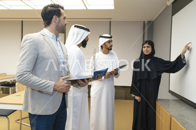 أستاذه جامعيه عربيه إماراتية خليجيه تشرح لطلابها المحاضره, مدربه جامعيه,طلاب إماراتيون يقفنا أمام الأستاذة ويتم  تدوين الملاحظات على جهاز الحاسب , التعليم الجامعي في الإمارات العربية المتحدة , فريق عمل عربي إماراتي  خليجي