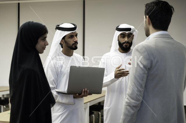 صورة بلون الاسود والابيض لأستاذ جامعي عربي إماراتي خليجي يشرح لطلابه المحاضره, طلاب إماراتيون يقفنا أمام الاستاذ و يتم تدوين الملاحظات على جهاز الحاسب , فريق عمل عربي إماراتي  خليجي, الإجتماع في مقر العمل, مناقشة مهام العمل, تحقيق الأهداف, تدريب الموظفين,