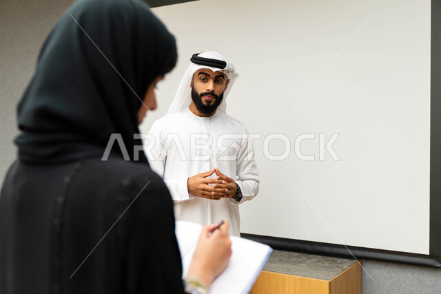 أستاذ جامعي عربي إماراتي خليجي يشرح لطلابه المحاضره, مدرب جامعي, تدوين الملاحظات على السبوره, التعليم الجامعي في الإمارات العربية المتحدة , فريق عمل عربي إماراتي خليجي, الإجتماع في مقر العمل, مناقشة مهام العمل, تحقيق الأهداف, تدريب الموظفين, ورشة عمل