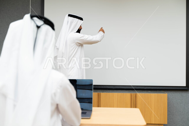 أستاذ جامعي عربي إماراتي خليجي يشرح لطلابه المحاضره, مدرب جامعي, تدوين الملاحظات على السبوره, التعليم الجامعي في الإمارات العربية المتحدة , فريق عمل عربي إماراتي خليجي, الإجتماع في مقر العمل, مناقشة مهام العمل, تحقيق الأهداف, تدريب الموظفين, ورشة عمل