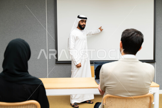 أستاذ جامعي عربي إماراتي خليجي يشرح لطلابه المحاضره, مدرب جامعي, تدوين الملاحظات على السبوره, التعليم الجامعي في الإمارات العربية المتحدة , فريق عمل عربي إماراتي خليجي, الإجتماع في مقر العمل, مناقشة مهام العمل, تحقيق الأهداف, تدريب الموظفين, ورشة عمل