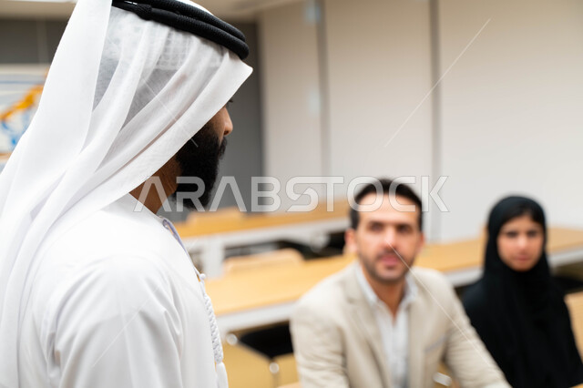 أستاذ جامعي عربي إماراتي خليجي يشرح لطلابه المحاضره, مدرب جامعي, تدوين الملاحظات على السبوره, التعليم الجامعي في الإمارات العربية المتحدة , فريق عمل عربي إماراتي خليجي, الإجتماع في مقر العمل, مناقشة مهام العمل, تحقيق الأهداف, تدريب الموظفين, ورشة عمل