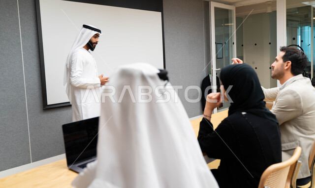 أستاذ جامعي عربي إماراتي خليجي يشرح لطلابه المحاضره, مدرب جامعي, تدوين الملاحظات على السبوره, التعليم الجامعي في الإمارات العربية المتحدة , فريق عمل عربي إماراتي خليجي, الإجتماع في مقر العمل, مناقشة مهام العمل, تحقيق الأهداف, تدريب الموظفين, ورشة عمل