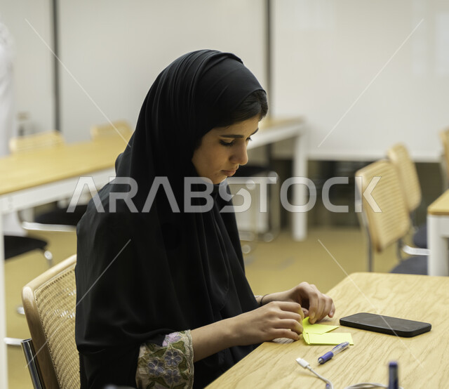 صوره مقربه لطالبه جامعيه عربيه إماراتيه  خليجيه في قاعة المحاضرات في الجامعه, طلاب جامعيين, تدوين الملاحظات, الإستماع الى المحاضره, ورش عمل, دورات تدريبيه, دروس و محاضرات, جودة التعليم
