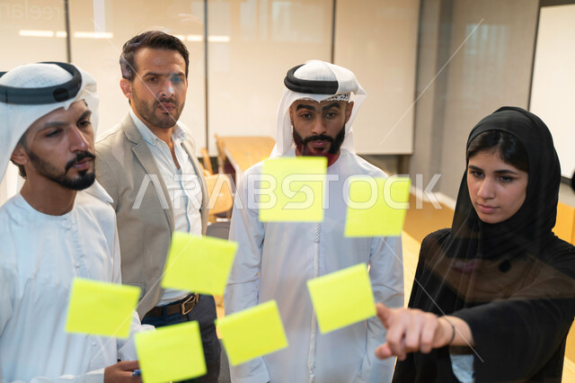 A team of Arab Emirati Gulf male and female students at the university headquarters, taking notes and tasks on paper, discussing and setting goals, using the laptop, university professors, discussing a project, university education, university trainers, t