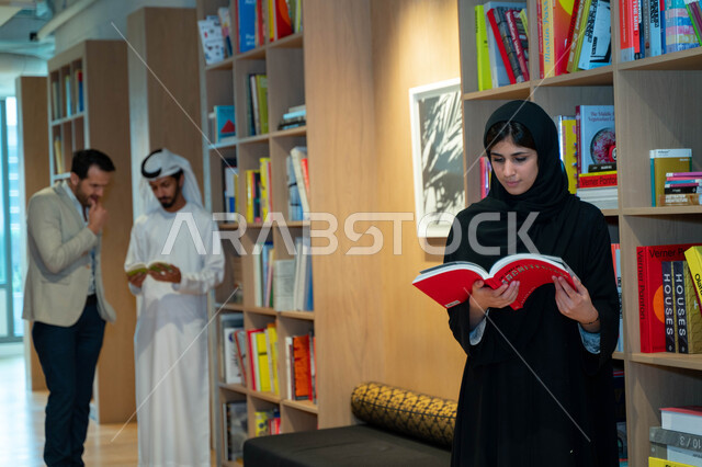 طلاب عرب خليجين إماراتين في مكتبة الجامعة، قراءة كتاب داخل المكتبة، تدوين الملاحظات, استعارة كتاب مناسب، الدراسه في مكتبة الجامعه, اثراء التعليم الجامعي، البحث العلمي، مفهوم العلم والتعلم