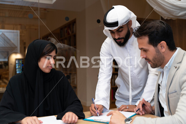 A group of Emirati Gulf Arab female and male students at the university, sharing academic information, discussing academic materials, group project, scientific research, university trainers, working group meeting within the company, defining work strategi