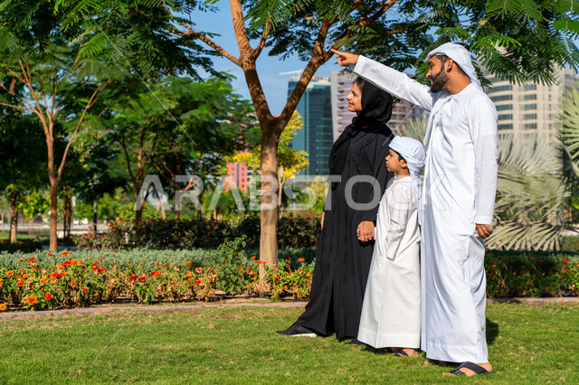 عائله عربيه إماراتية خليجيه مكونه من ثلاث أفراد, أب إماراتي يأشر بيده  الى الأعلى , قضاء وقت ممتع في الحديقه, رحله عائليه, مفهوم الأسره السعيده, إجازه صيفيه, الاستمتاع باللعب الجماعي في المنتزه, تسليه وترفيه