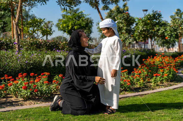 طفل عربي إماراتي خليجي يلعب مع والدته في المنتزه, أم إماراتيه  تنظر  الى  إبنها بكل حب وحنان  في الحديقه, الإستمتاع باللعب في يوم مشمس, قضاء وقت ممتع مع الابناء, رحله عائليه, اللعب الجماعي, مفهوم الأسره السعيده, تسليه وترفيه, عطلة نهاية الأسبوع