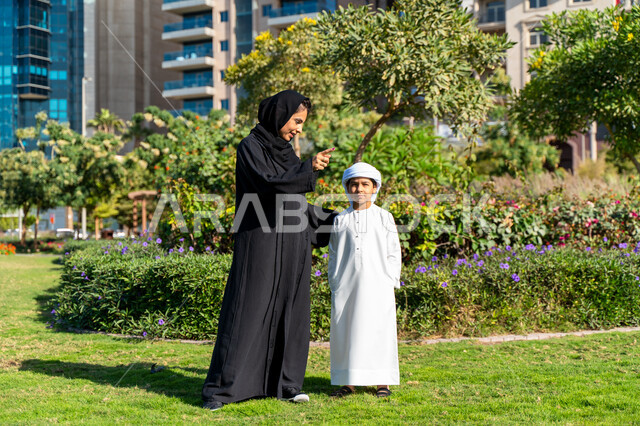 An Arab Emirati Gulf child playing with his mother in the park, a mother embracing her son in the garden, enjoying playing on a sunny day, spending quality time with children, family trip, group play, happy family concept, entertainment, weekend