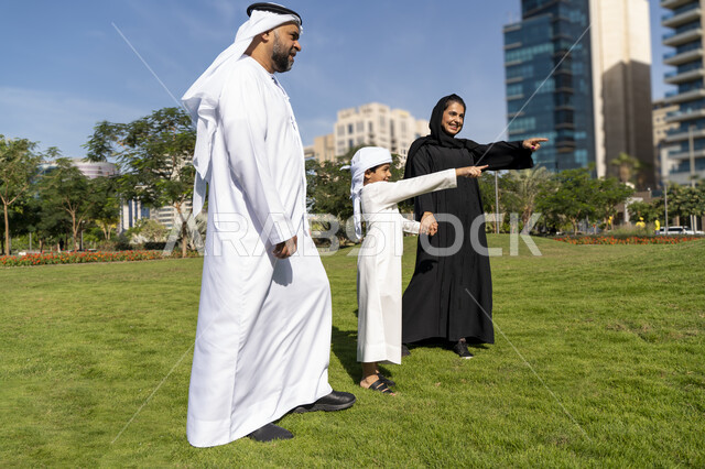 عائله عربيه إماراتية خليجيه مكونه من ثلاث أفراد, أب وأم إماراتيان يمسكان يد طفلهم, قضاء وقت ممتع في الحديقه , رحله عائليه, مفهوم الأسره السعيده, إجازه صيفيه, الاستمتاع باللعب الجماعي في المنتزه, تسليه وترفيه