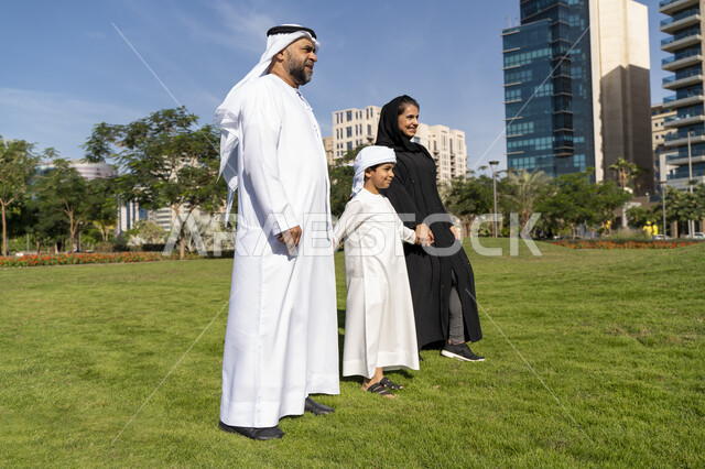 عائله عربيه إماراتية خليجيه مكونه من ثلاث أفراد, أب وأم إماراتيان يمسكان يد طفلهم, قضاء وقت ممتع في الحديقه , رحله عائليه, مفهوم الأسره السعيده, إجازه صيفيه, الاستمتاع باللعب الجماعي في المنتزه, تسليه وترفيه