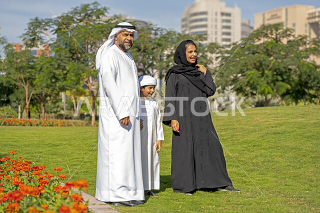 عائله عربيه إماراتية خليجيه مكونه من ثلاث أفراد, أب وأم إماراتيان يمسكان يد طفلهم, قضاء وقت ممتع في الحديقه , رحله عائليه, مفهوم الأسره السعيده, إجازه صيفيه, الاستمتاع باللعب الجماعي في المنتزه, تسليه وترفيه