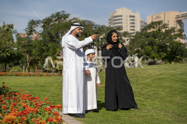 عائله عربيه إماراتية خليجيه مكونه من ثلاث أفراد, أب وأم إماراتيان يمسكان يد طفلهم, قضاء وقت ممتع في الحديقه , رحله عائليه, مفهوم الأسره السعيده, إجازه صيفيه, الاستمتاع باللعب الجماعي في المنتزه, تسليه وترفيه